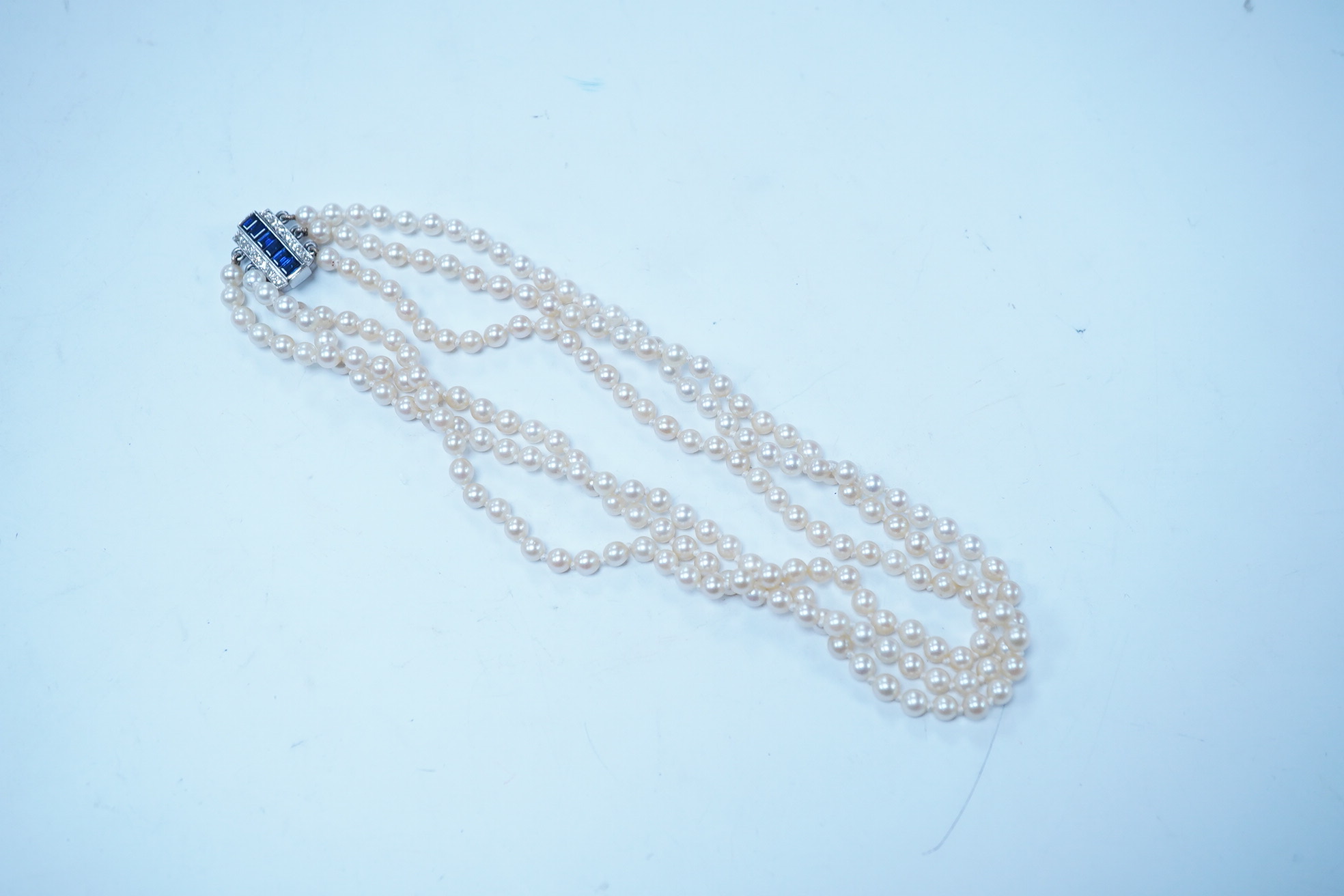 A triple strand cultured pearl choker necklace, with sapphire and diamond cluster set rectangular white metal clasp, 32cm. Condition - fair to good